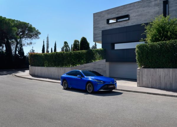 Blaues Wasserstoffauto steht geparkt vor einem modernen Einfamilienhaus.