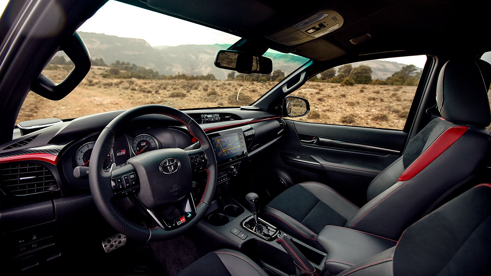 Innenraum des Toyota Hilux im Frontbereich, mit dunklen Sitzen und roten Akzenten