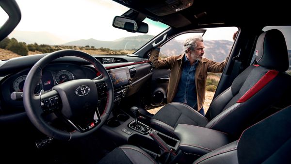 Vorderere Innenraum eines Toyota Hilux, in der Beifahrertür lehnt ein Mann in Lederjacke