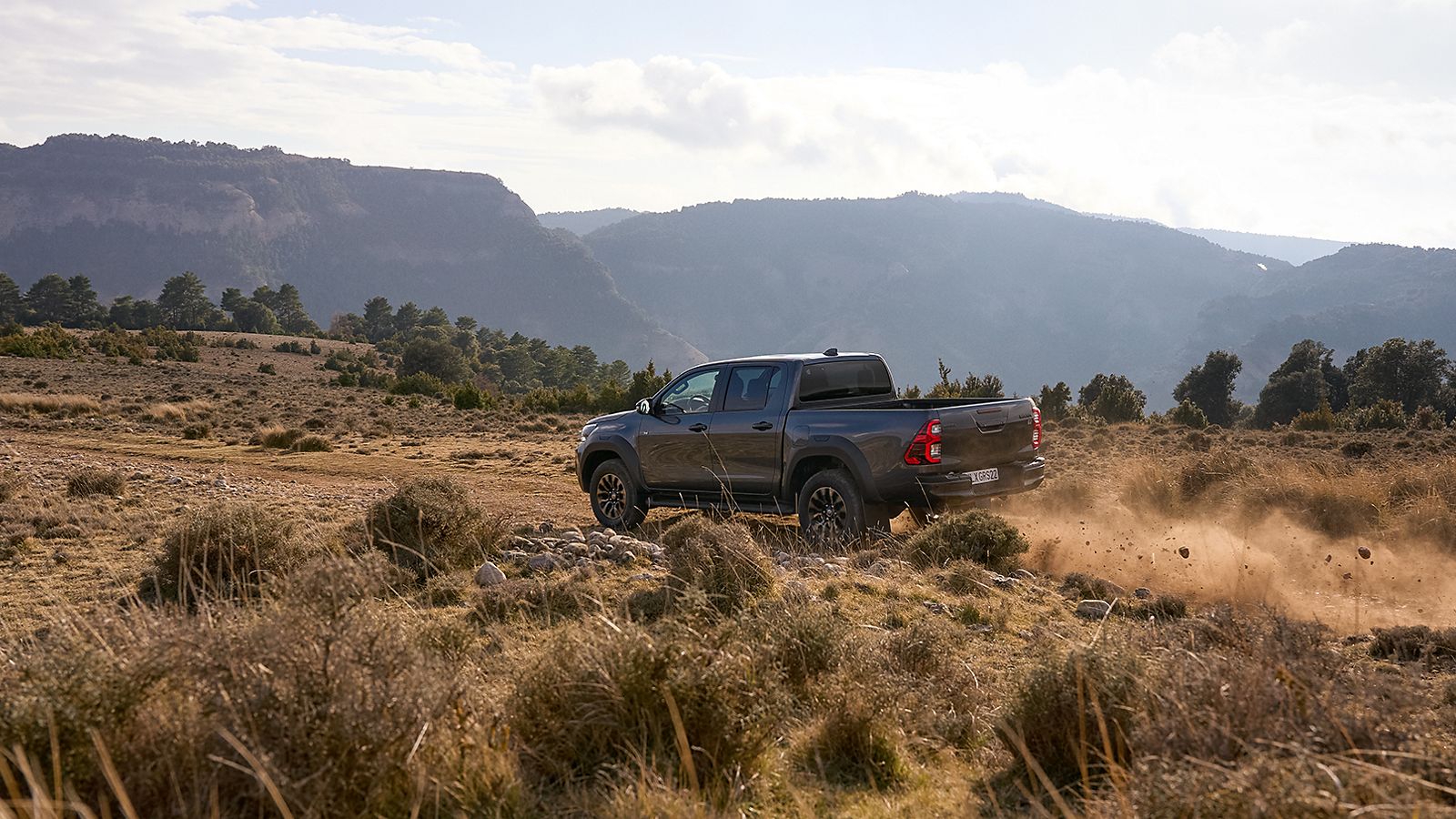 Toyota Hilux fährt auf einer staubigen Straße in einer gelbgrünen Graslandschaft