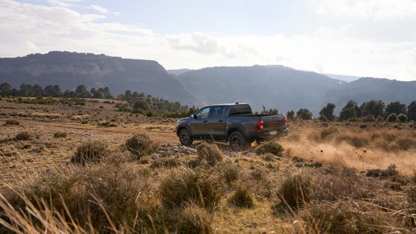 Toyota Hilux fährt auf einer staubigen Straße in einer gelbgrünen Graslandschaft