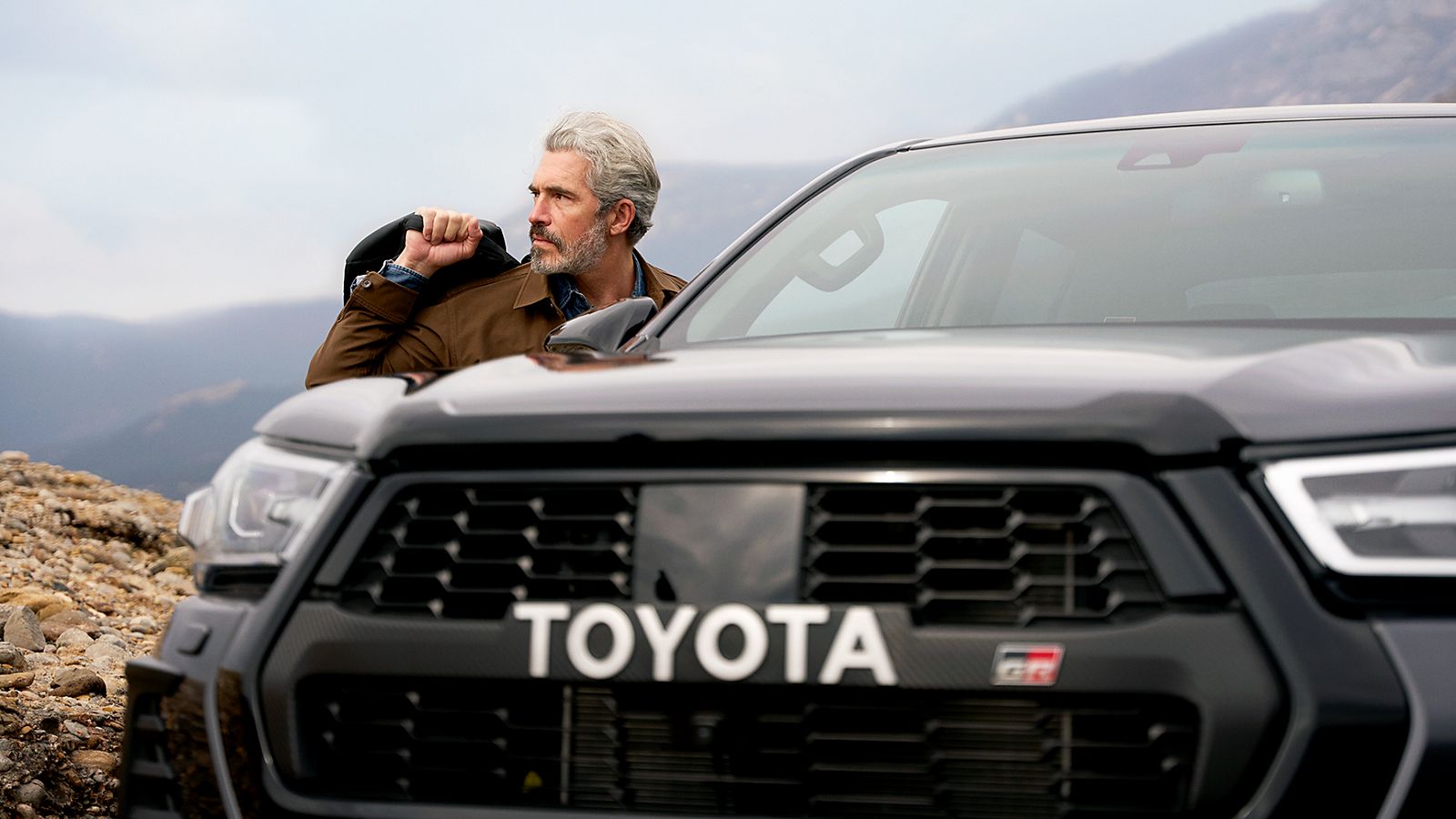 Toyota Hilux von vorne, während sich ein Mann links eine Jacke anzieht