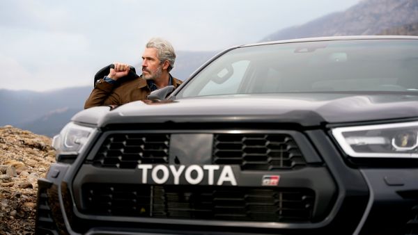 Toyota Hilux von vorne, während sich ein Mann links eine Jacke anzieht