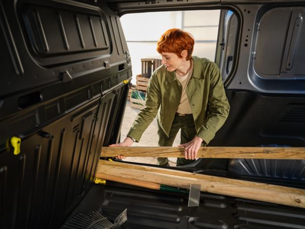 Eine Person mit kurzen roten Haaren lädt vorsichtig Holzbretter in den Kofferraum eines Lieferwagens und demonstriert damit die effiziente Nutzung des Laderaums.