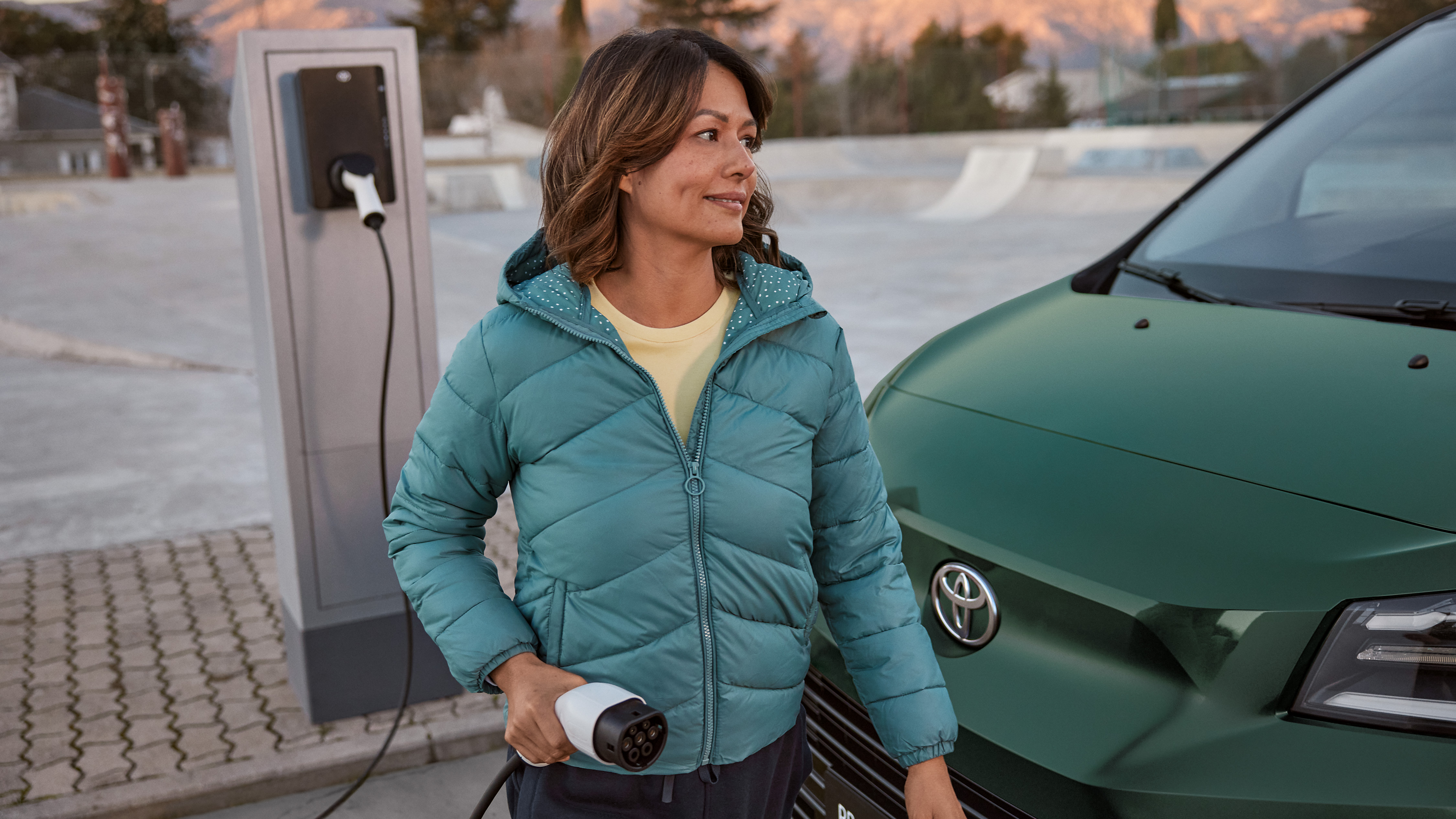 Grünes E-Auto wird gerade von einer Person an eine Wallbox angeschlossen.