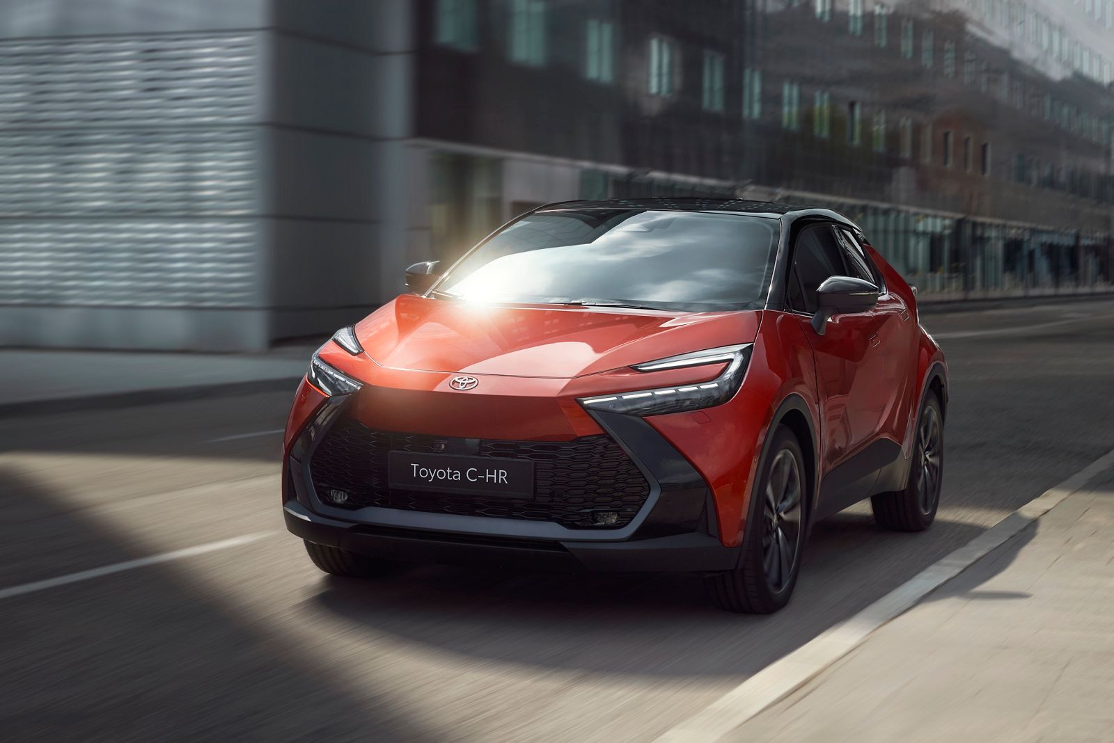 Modern binalar arasında yol alan kırmızı Toyota C-HR dinamik tasarımıyla hareket halinde