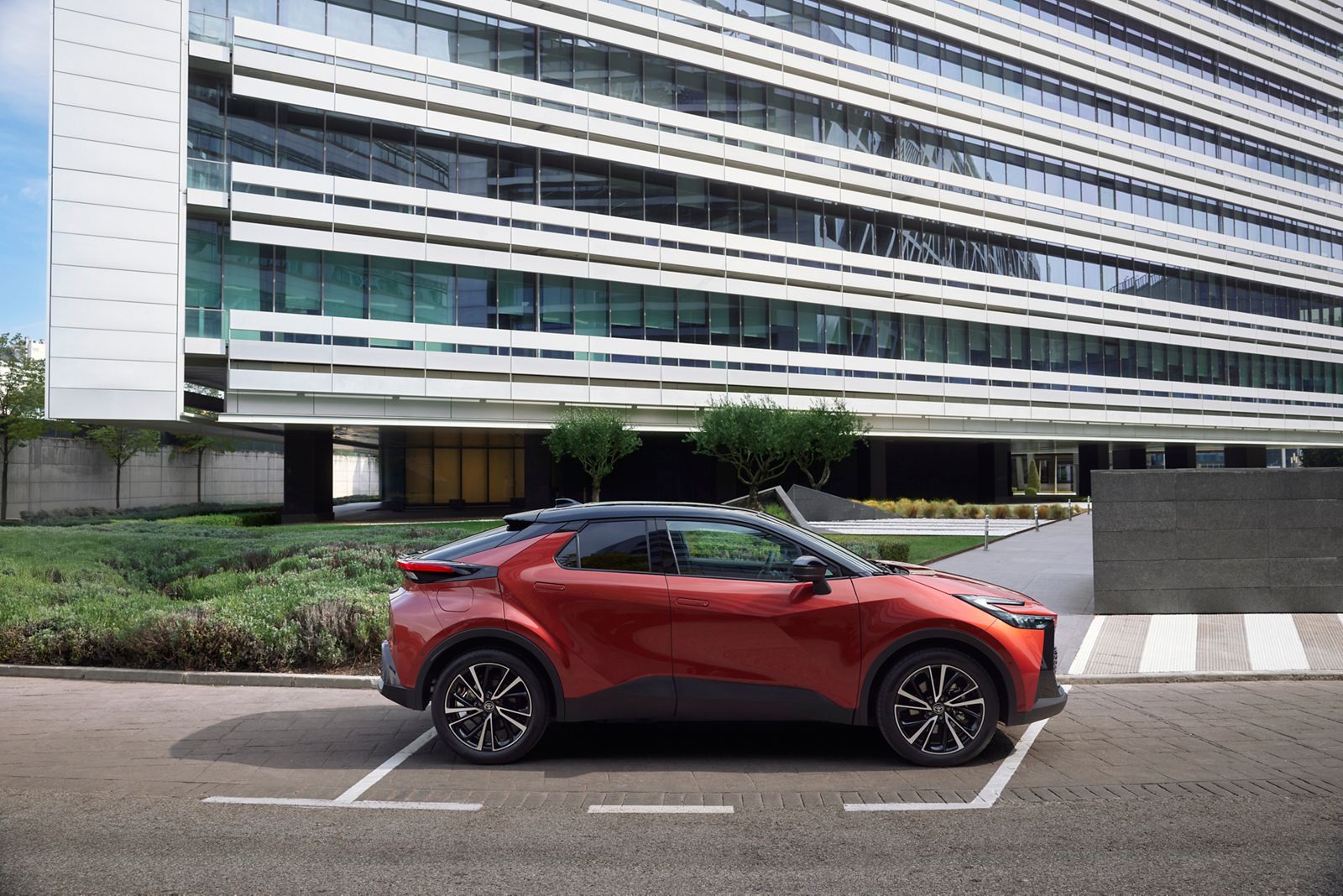 Geniş cam cepheli bir bina önünde park halinde duran kırmızı Toyota C-HR yan görünümü