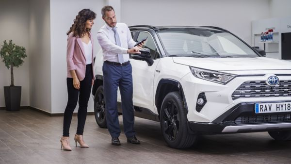 Konsultacja klientki z doradcą w salonie Toyoty przy białym modelu RAV4 Hybrid, w nowoczesnym wnętrzu
