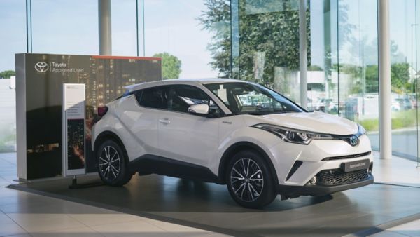 Biała Toyota C-HR Hybrid prezentowana w salonie jako certyfikowany pojazd używany, na tle przeszklonego wnętrza 