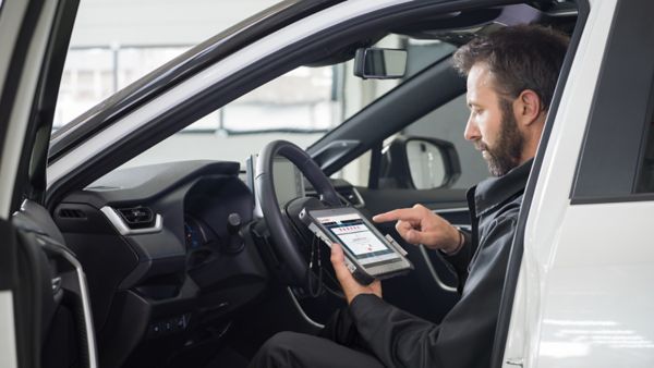 Technik w ciemnej kurtce wykonuje diagnostykę pojazdu za pomocą tabletu w kabinie białej Toyoty, analizując dane na ekranie