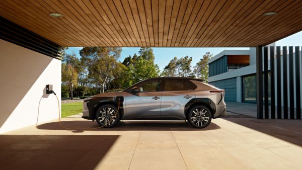 Elektryczny SUV Toyota bZ4X pod drewnianą wiatą, podłączony do domowej ładowarki ściennej