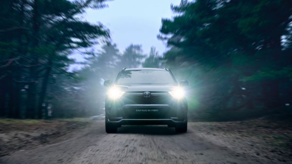Toyota RAV4 Plug-in Hybrid z zapalonymi przednimi światłami podczas podróży przez zalesiony teren