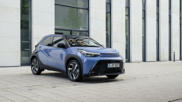 Zdjęcie błękitnej Toyoty Aygo X zaparkowanej obok nowoczesnego budynku