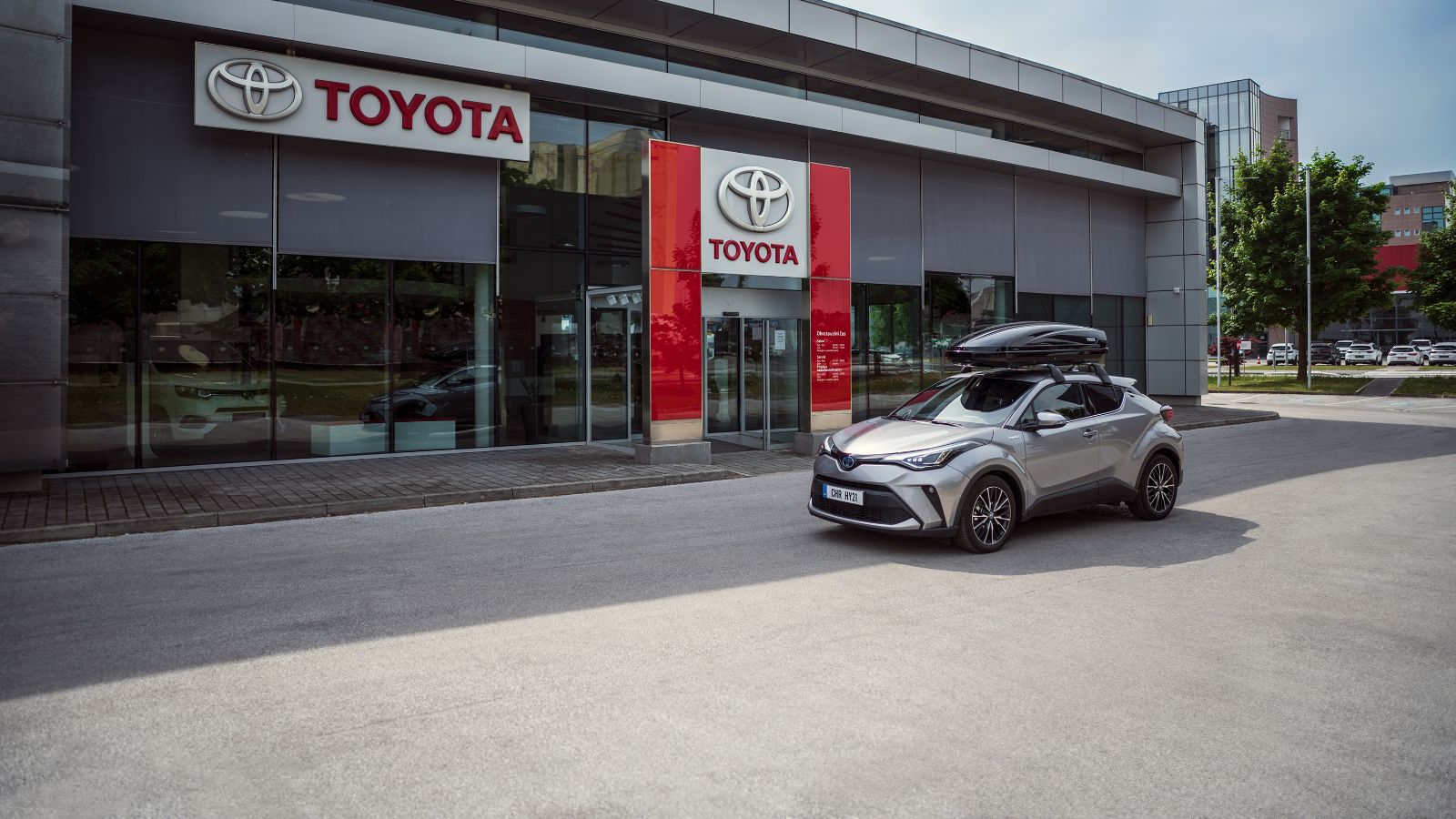 Srebrna Toyota z bagażnikiem dachowym zaparkowana przed salonem Toyoty