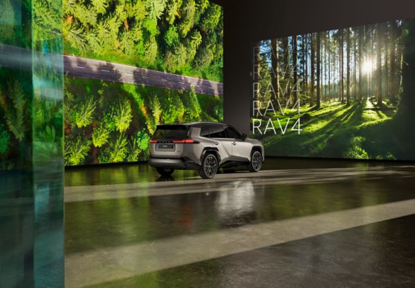 RAV4 hybride rechargeable garé devant des écrans montrant des images de forêt