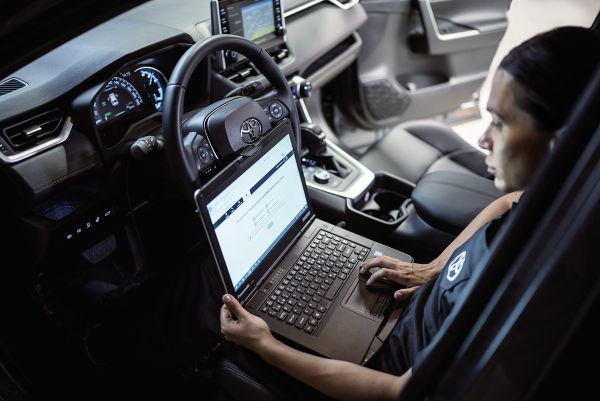 Zwei Toyota-Mechaniker arbeiten an einem Auto, einer im Innenraum, einer an der geöffneten Motorhaube.