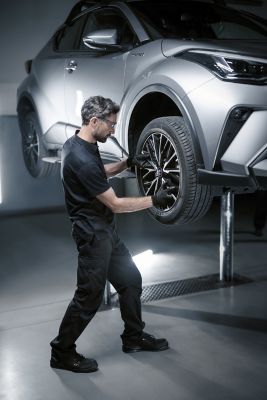Ein Werkstattmitarbeiter in Arbeitskleidung beugt sich über den Motorraum und bedient ein auf dem Motorblock abgestelltes Laptop.