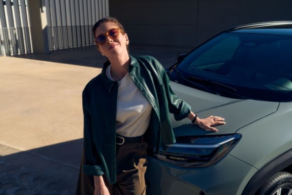 Eine junge Frau steht lässig neben einem Fahrzeug, das als Firmenauto genutzt wird und für den Sachbezug in Österreich relevant ist.