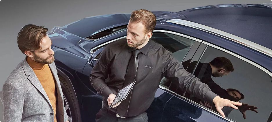 Dwóch eleganckich mężczyzn rozmawia obok szaroniebieskiego Lexusa