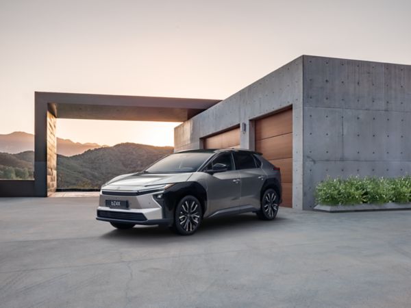 Silberner Toyota bZ4X Elektro-SUV steht vor einem brutalistischen Beton-Gebäude, im Hintergrund geht die Sonne gerade unter.