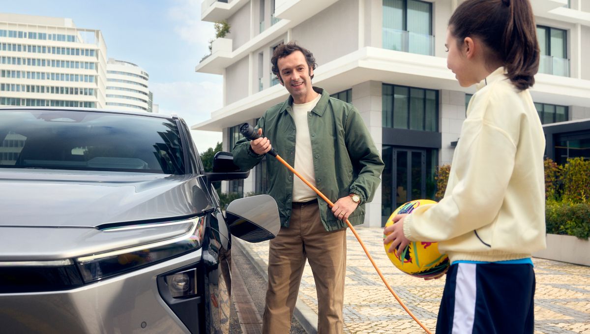 Person hält Ladekabel an einem Toyota bZ4X, im Hintergrund Wohngebäude und gepflasterter Hofbereich.
