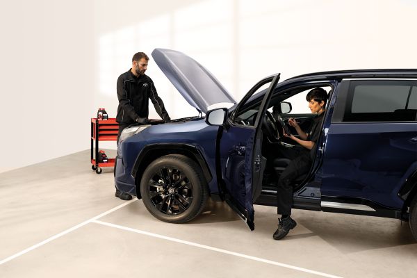 Zwei Toyota-Mechaniker arbeiten an einem Auto, einer im Innenraum, einer an der geöffneten Motorhaube.