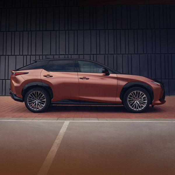 Seitenansicht eines kupferfarbenen Lexus RZ neben einem Tennisfeld