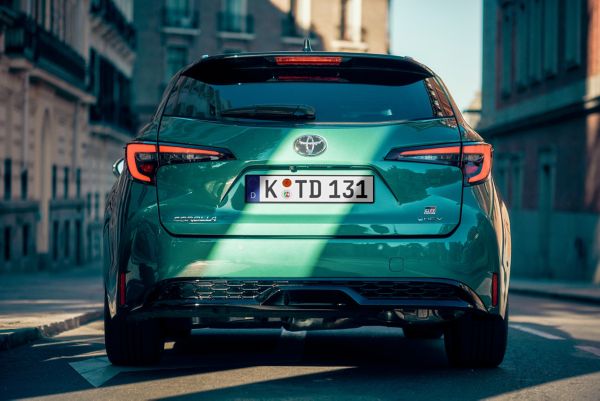 Rückansicht eines grünen Corolla GR Sport, geparkt in der Stadt, die Bremsleuchten sind aktiv, ein Streifen Sonnenlicht fällt auf die Heckklappe