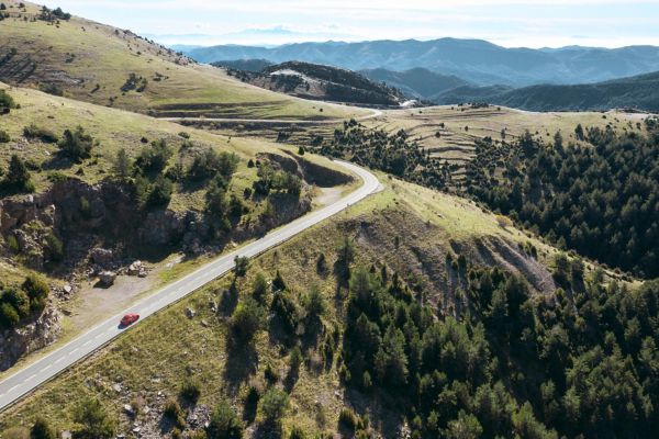 Luftaufnahme eines roten GR Supra auf einer kurvigen Landstraße in teilweise baumloser Berglandschaft