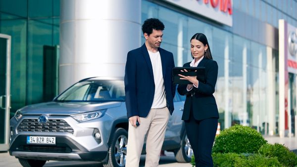 Suv model Toyota aracın önünde duran ve tablete bakan bir adam ve kadın