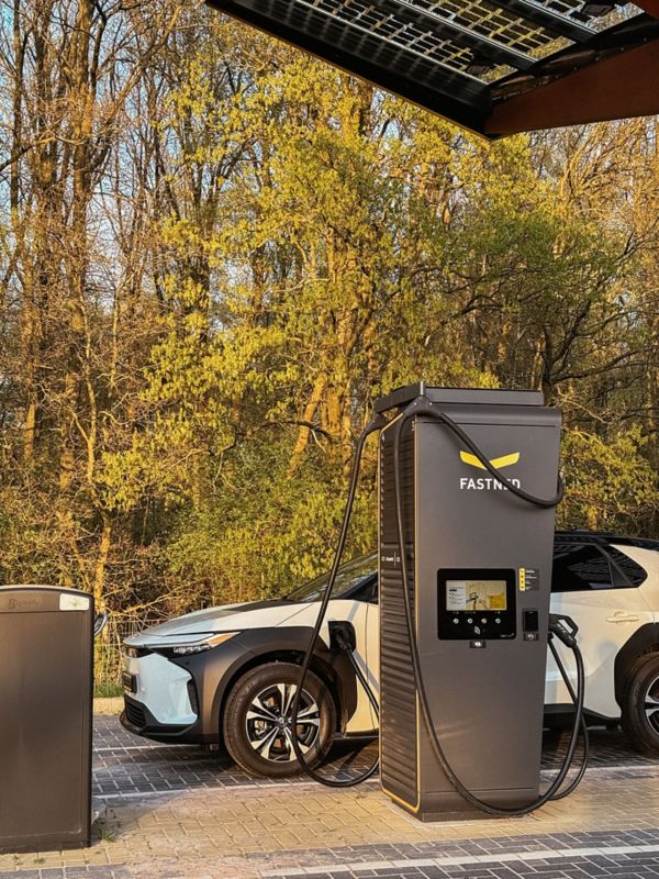 Toyota bZ4X aan snellaadstation zijaanzicht voor bomen
