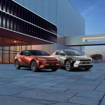 Eine Frau steckt den Ladestecker in einen grau-schwarzen Toyota C-HR, im Hintergrund eine Wallbox, Bildtext: „STECKERFAHRZEUGE MIT 0%-FINANZIERUNG“