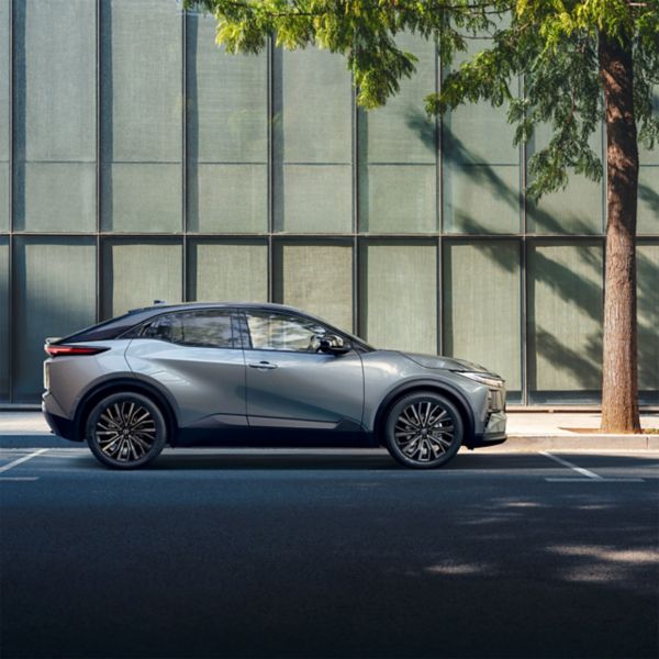 Toyota C-HR+ rijdt voor een gebouw langs