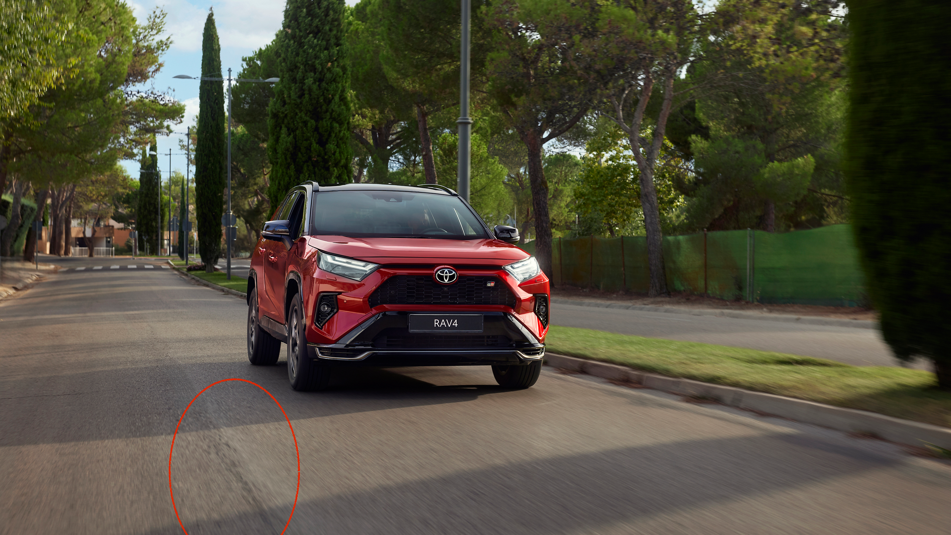 Roter RAV4 fährt auf einer mit Bäumen gesäumten Landstraße entlang.