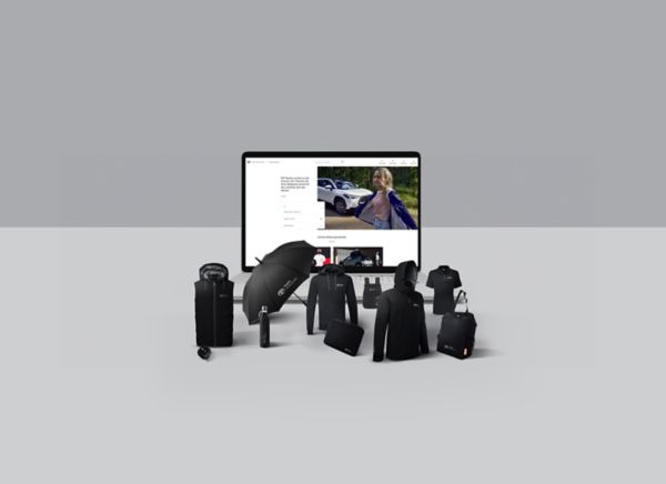 Einige schwarze Toyota-Merchandise-Artikel, darunter Schirm, Jacke und Trinkflasche sind neben einem Bildschirm angeordnet, der eine Website mit einem Toyota RAV4 im Schnee zeigt. 
