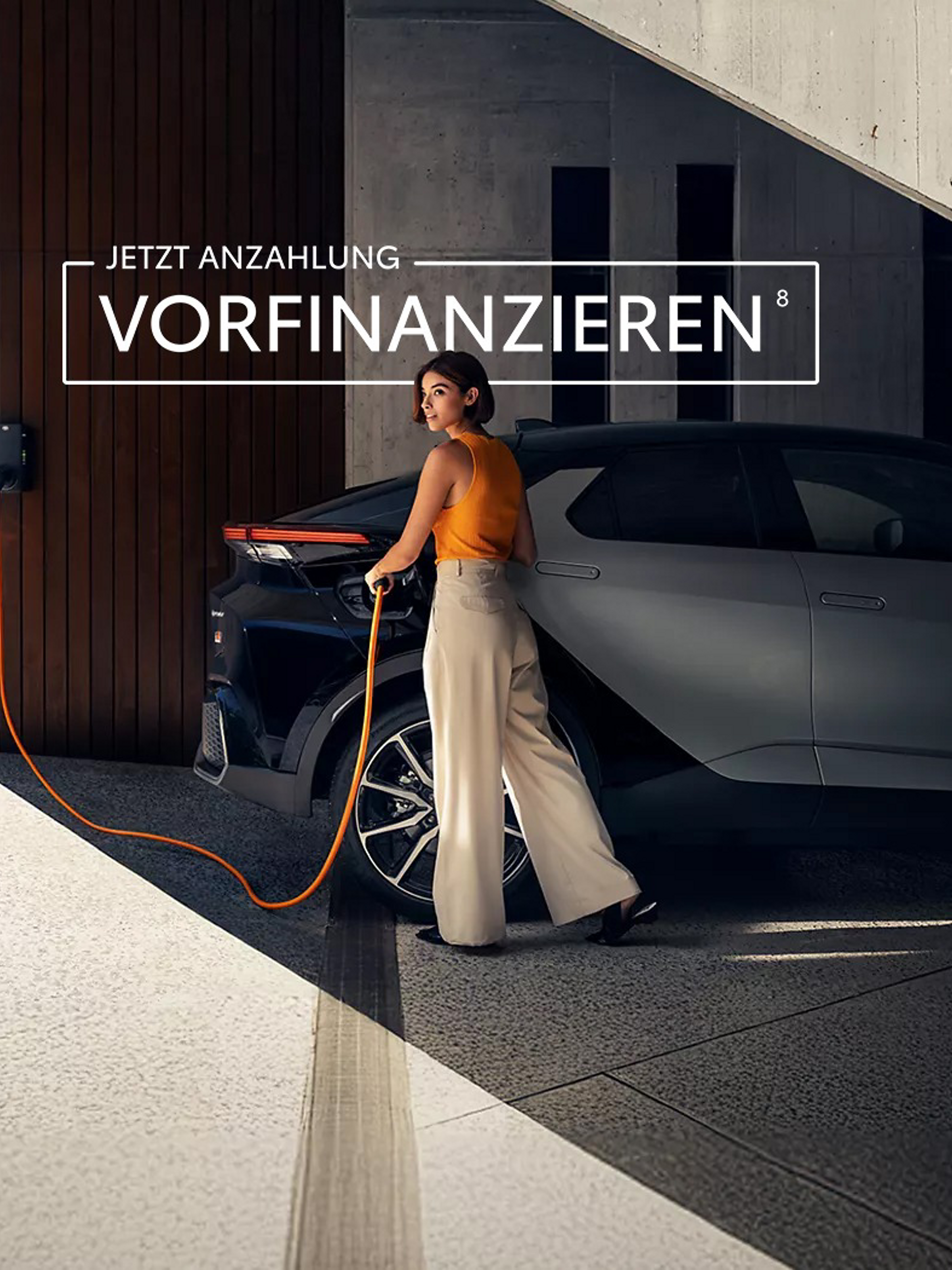 Frau lädt einen C-HR mit Ladekabel an einer Wallbox in einer modernen, architektonischen Garage.