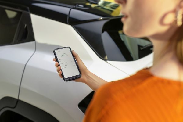 Person mit orangenem Pullover steht mit einem Smartphone in der Hand vor einem weißen Urban Cruiser.