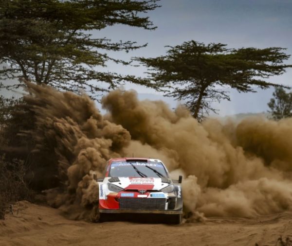 Ein Rallye-Auto rast durch staubiges Gelände und wirbelt eine große Staubwolke auf, während es einen anspruchsvollen Parcours bewältigt.