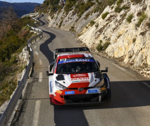 Ein rot-weißes Rallye-Auto navigiert eine kurvenreiche Bergstraße entlang und zeigt die Spannung des Motorsports.