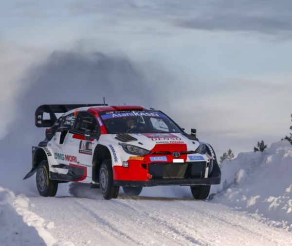 Ein Rallye-Auto fliegt förmlich über ein schneebedecktes Gelände und wirbelt dabei Schnee auf. Das Bild betont Geschwindigkeit und Wendigkeit unter schwierigen Bedingungen.