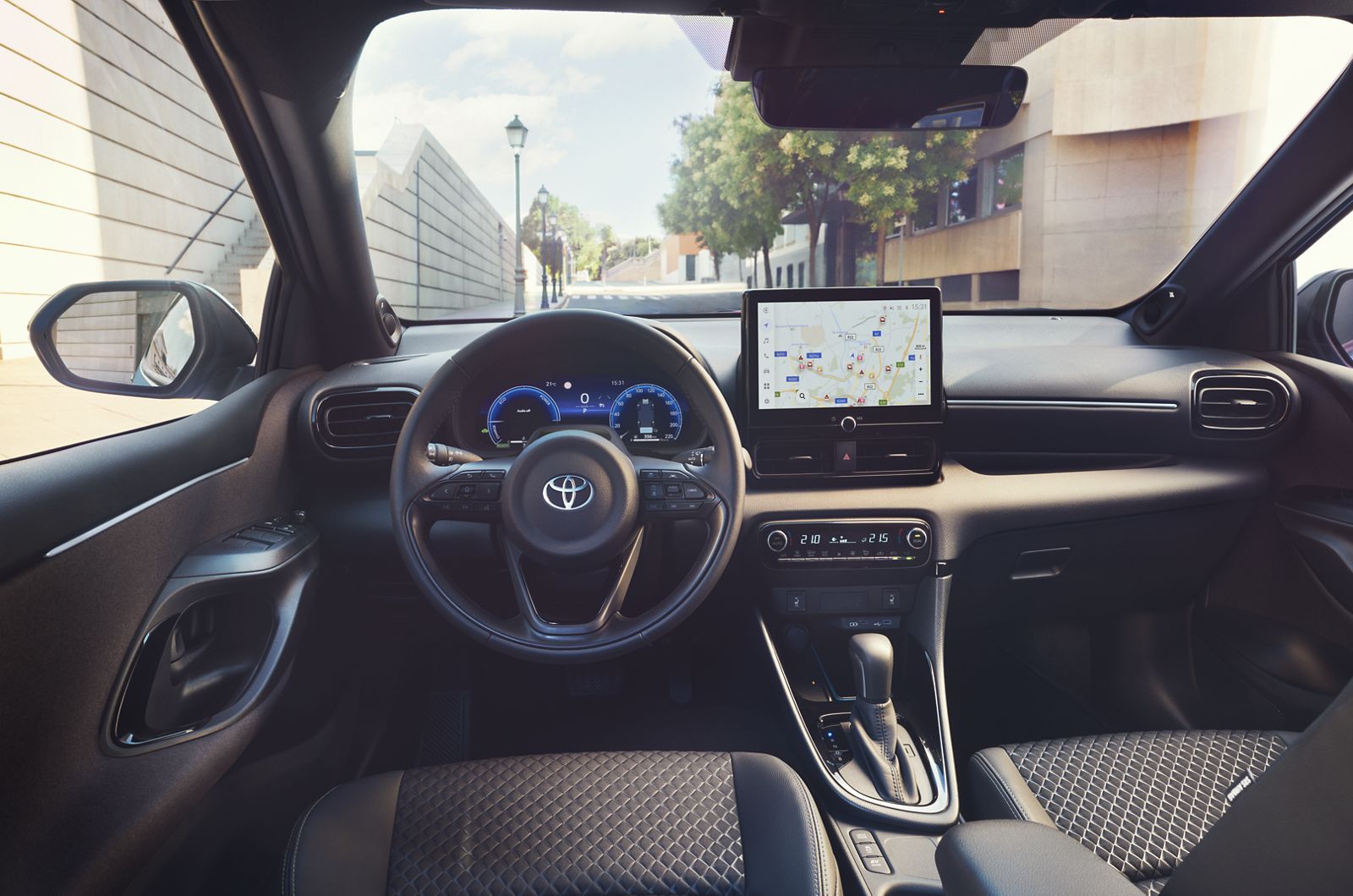 Cockpit des Yaris mit Kartenanzeige auf dem Multimedia-Bildschirm, durch die Frontscheibe ist eine Straße mit Laternen, Bäumen und Häusern zu sehen