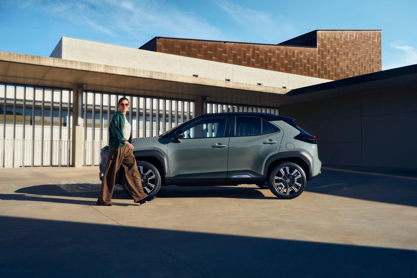 Vue latérale de la Yaris Cross garée, avec une femme marchant vers la voiture