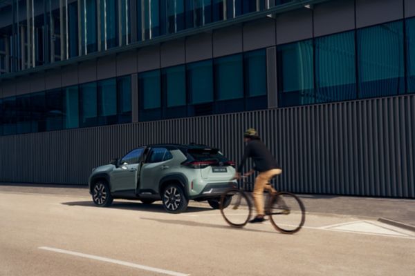 Toyota Corolla Cross geparkeerd naast een modern gebouw. Fietser rijdt voorbij