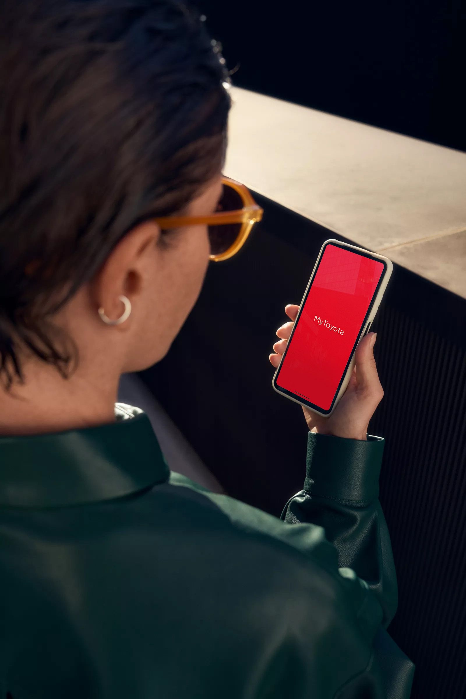 Blick über die Schulter einer Frau auf ein Smartphone, welches die Einstellungen der Klimaanlage eines Autos anzeigt.