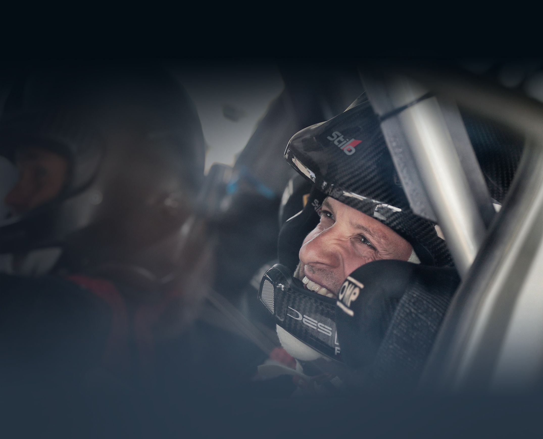 Zbliżenie uśmiechniętej twarzy kierowcy rajdowego w kasku siedzącego w samochodzie.