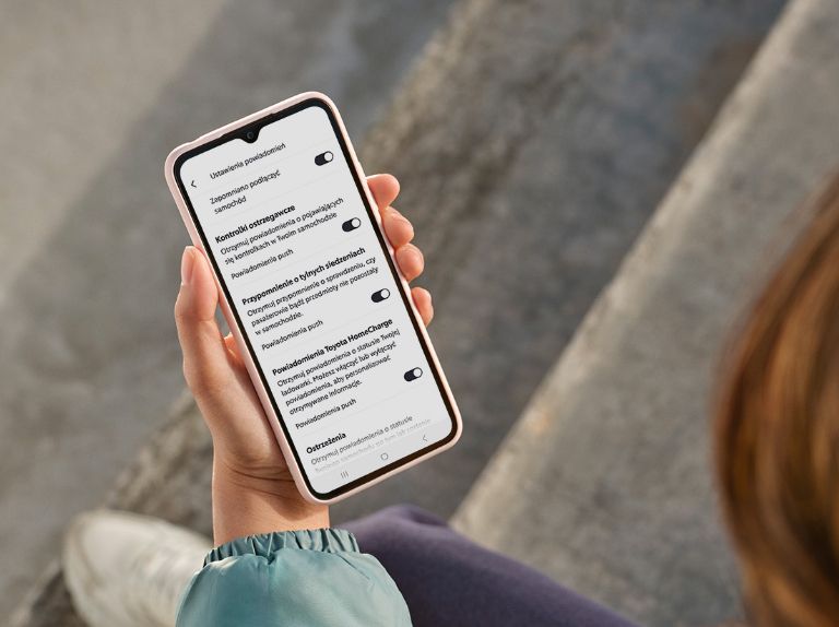 Dłoń trzymająca telefon z ustawieniami powiadomień na ekranie.