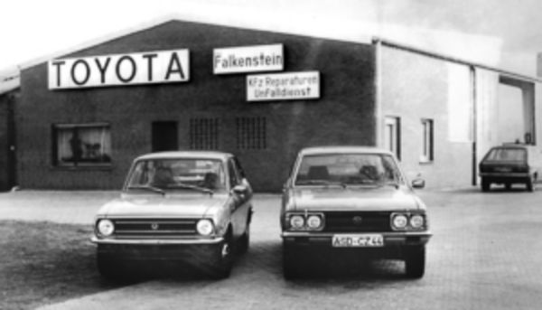 Ein Schwarzweiß-Bild von dem alten Autohaus Falkenstein mit zwei Fahrzeugen im Vordergrund