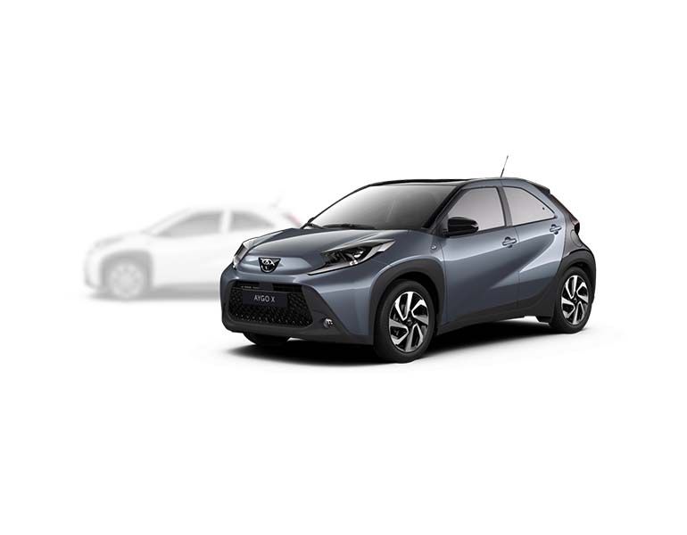 Grauer Toyota Aygo X steht diagonal zur Kamera, im Hintergrund ist unscharf ein heller Aygo X zu erkennen