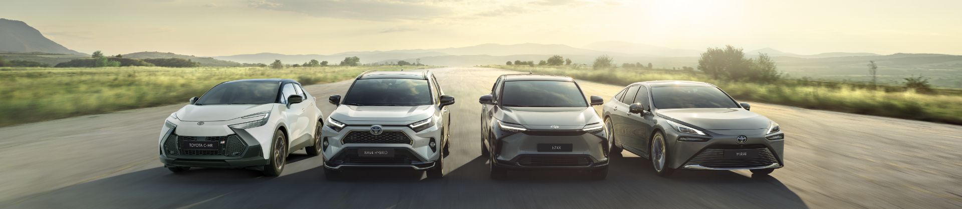Toyota C-HR, RAV4 Hybrid, Toyota bZ4X i Mirai jadą obok siebie drogą poza miastem.