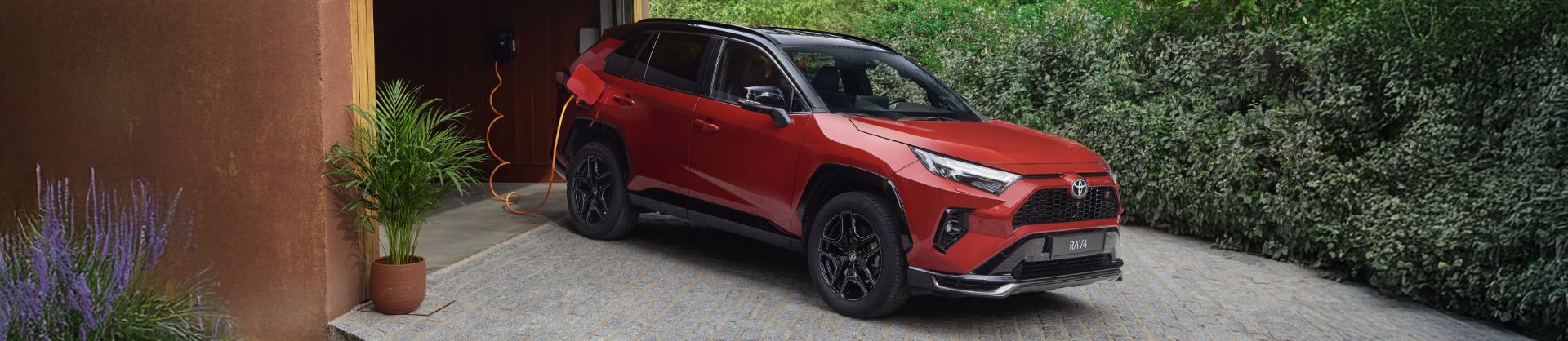 Toyota RAV4 Plug-in stoi przed posesją podczas ładowania ze stacji domowej.